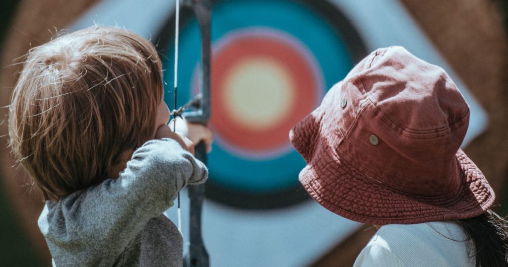 A bullseye target with two children learning archery